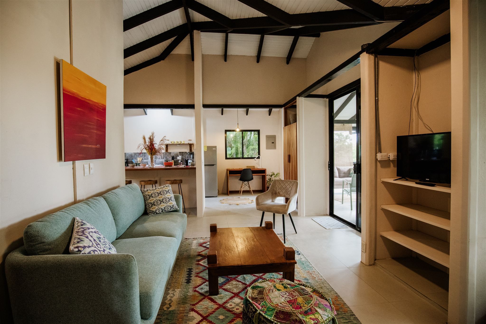 Living room with a sofa and TV, open to a kitchen with breakfast bar, a desk nook and a glass door to the terrace