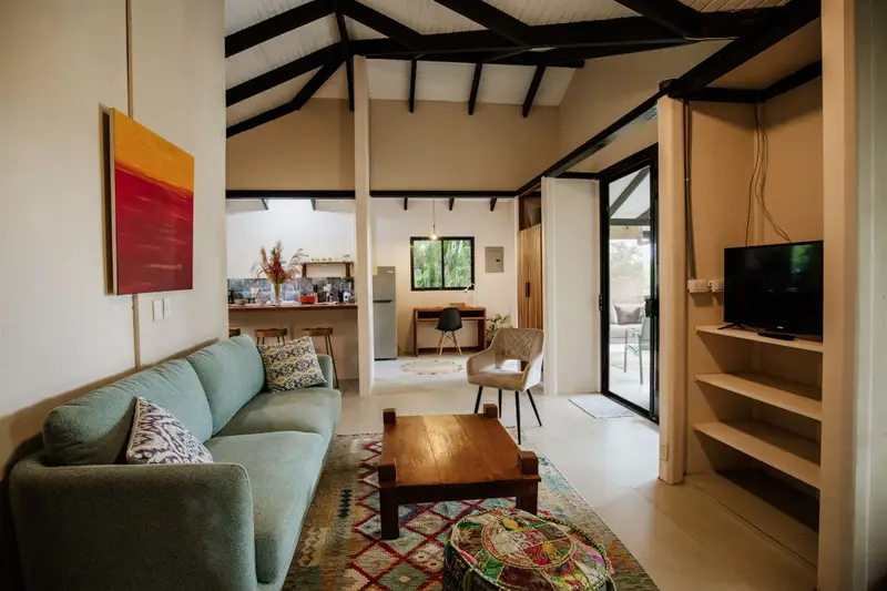 Living room with a sofa and TV, open to a kitchen with breakfast bar, a desk nook and a glass door to the terrace