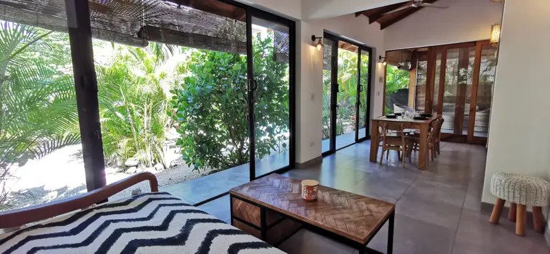 Living area with daybed, coffee table and dining table for four, glass sliding doors opening to a garden