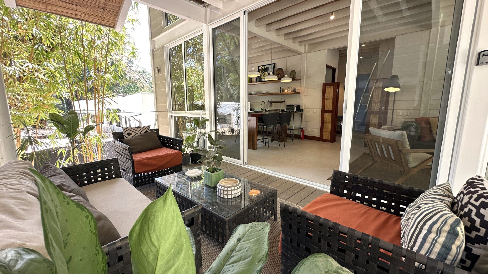 Covered terrace with wicker sofa and armchairs, glass doors open to a kitchen with bar stools