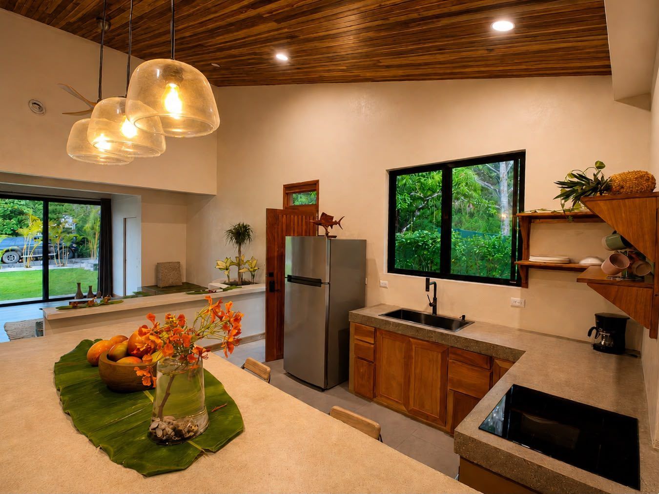 Kitchen with stainless fridge, sink, induction cooktop, coffee maker and a window onto trees