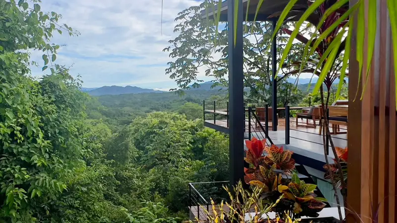 Covered deck with outdoor seating and railings overlooking a forested valley and distant mountains