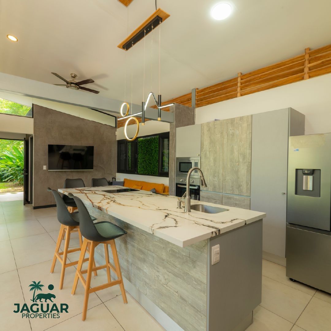 Open kitchen with marble island, bar stools, built-in oven and microwave, fridge, and a living area with wall TV