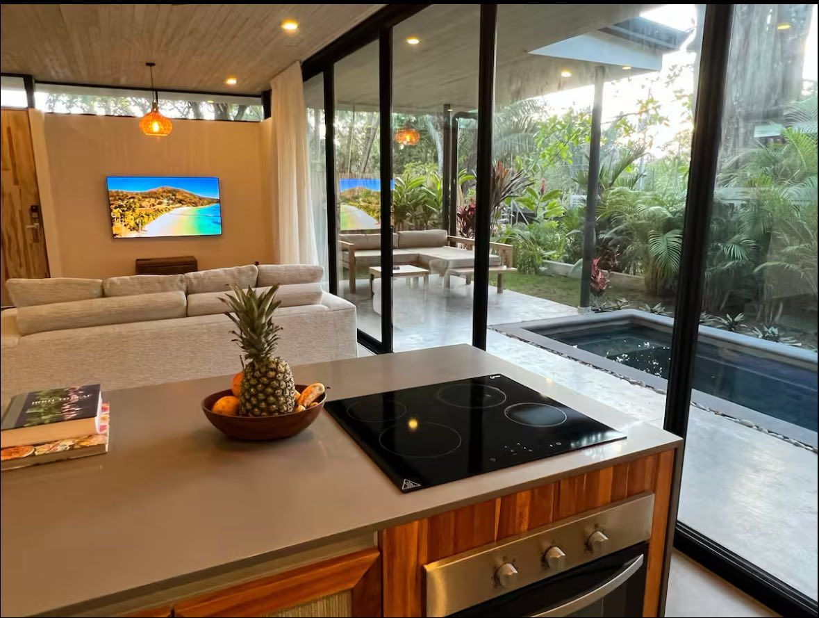 Kitchen island with induction cooktop and oven facing a living area with TV and sliding doors to a private pool